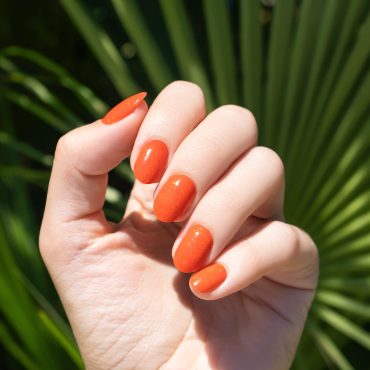Female hand with orange nail design. Orange nail polish manicure. Female hand on a tropic plant leaf background
